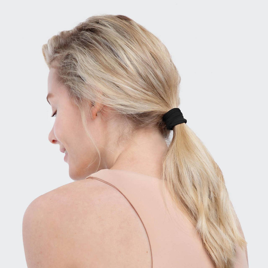 Femme blonde portant un élastique noir KITSCH en queue de cheval haute, accessoire doux sans couture pour cheveux.