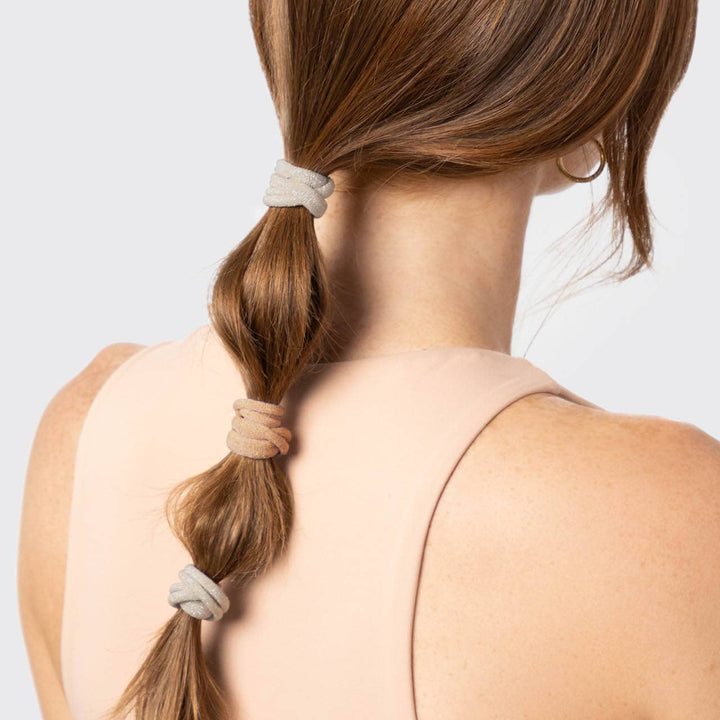 Femme aux cheveux bouclés portant des élastiques KITSCH pailletés tons neutres dans des couettes, coiffure tendance avec accessoires doux sans marques.