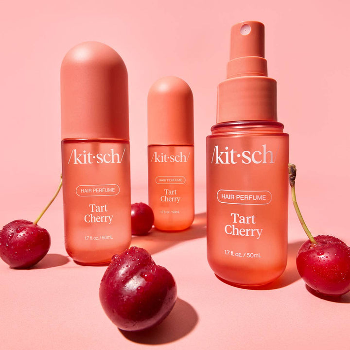 Collection du parfum pour cheveux KITSCH Cerise Acidulée avec flacons 50 ml et format vaporisateur, entourés de cerises fraîches sur fond rose. Parfum capillaire gourmand et fruité.