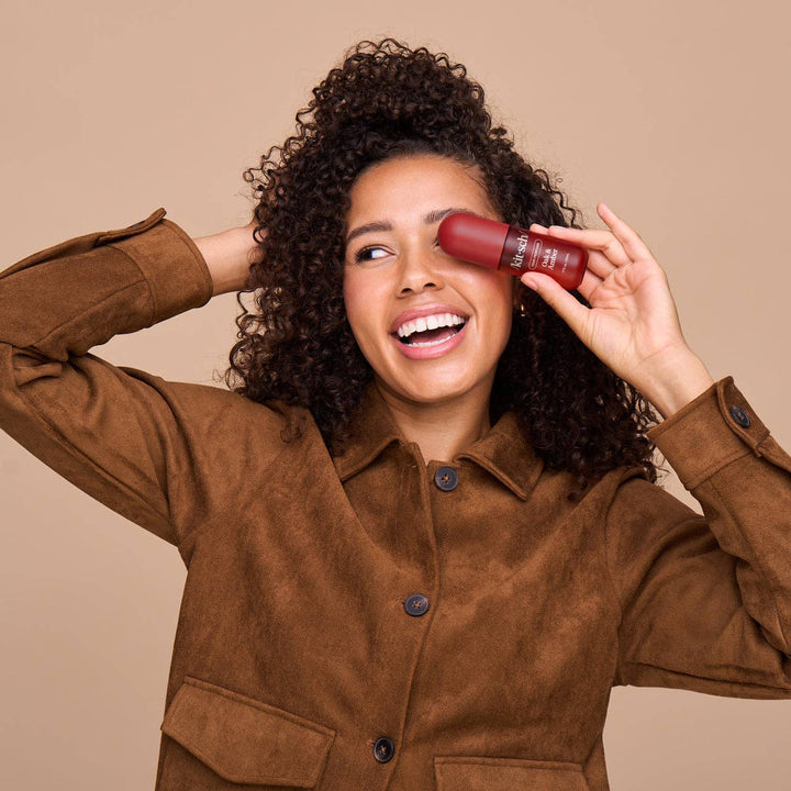 Femme souriante tenant le parfum pour cheveux KITSCH Chêne & Ambre, illustrant son utilisation quotidienne pour rafraîchir et parfumer les cheveux.
