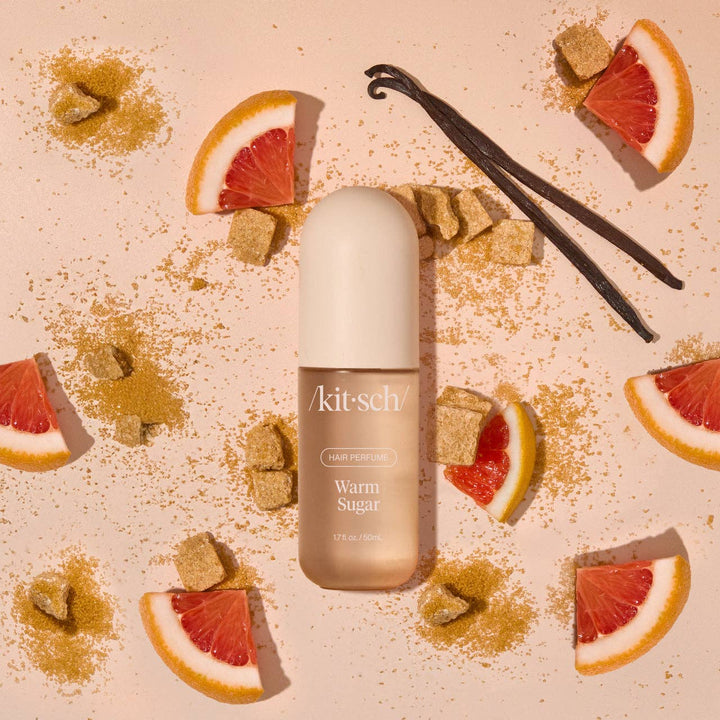 Parfum pour cheveux KITSCH Warm Sugar 50 ml posé sur un fond beige avec quartiers de pamplemousse, gousses de vanille et morceaux de sucre, ambiance gourmande.