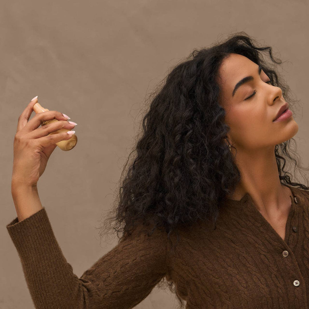 Femme aux cheveux bouclés vaporisant le parfum pour cheveux KITSCH Vanille Rustique. Brume légère parfumée pour rafraîchir les cheveux entre deux shampoings.
