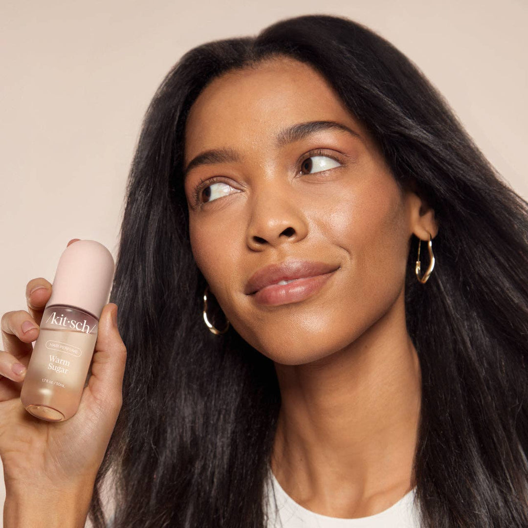 Personne tenant le parfum pour cheveux KITSCH Warm Sugar 50 ml dans la main avec des cheveux longs et brillants, démonstration d'utilisation du produit.