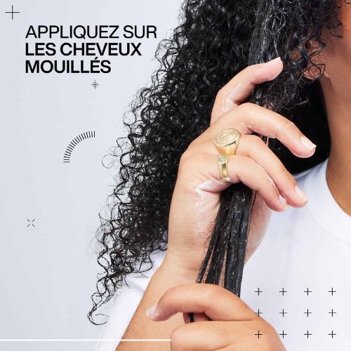 Main appliquant une crème coiffante sur cheveux bouclés mouillés pour définir et hydrater les boucles