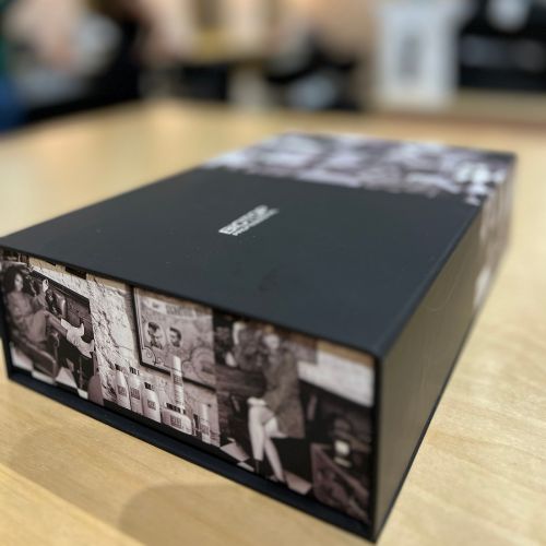 Coffret cadeau Biotop 911 fermé, de couleur noire avec visuel rétro noir et blanc sur les côtés, posé sur une table en bois clair. Packaging élégant et professionnel, idéal pour offrir un soin capillaire complet aux cheveux secs ou abîmés.