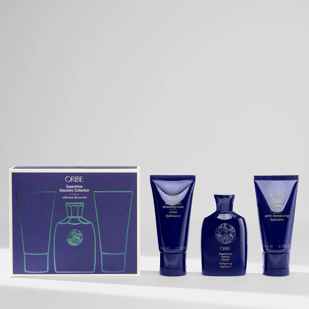 Coffret Oribe Supershine Discovery Collection avec shampooing hydratant, revitalisant et crème sans rinçage formats voyage disposés à côté de la boîte du coffret bleu signature.
