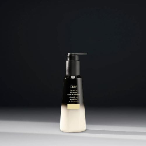 Crème de nuit capillaire réparatrice en flacon, posée sur un oreiller blanc avec des mèches de cheveux brillants en arrière-plan.