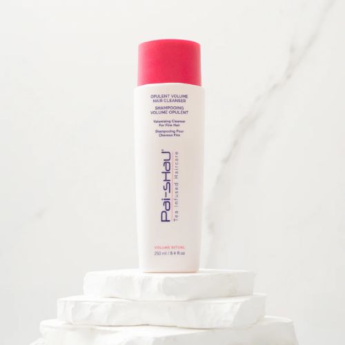 Flacon blanc mat de 250 ml du Revitalisant Volume Opulent Pai-Shau avec bouchon rose, posé sur des pierres blanches. Soin capillaire volumisant végétalien, pour cheveux fins ou colorés
