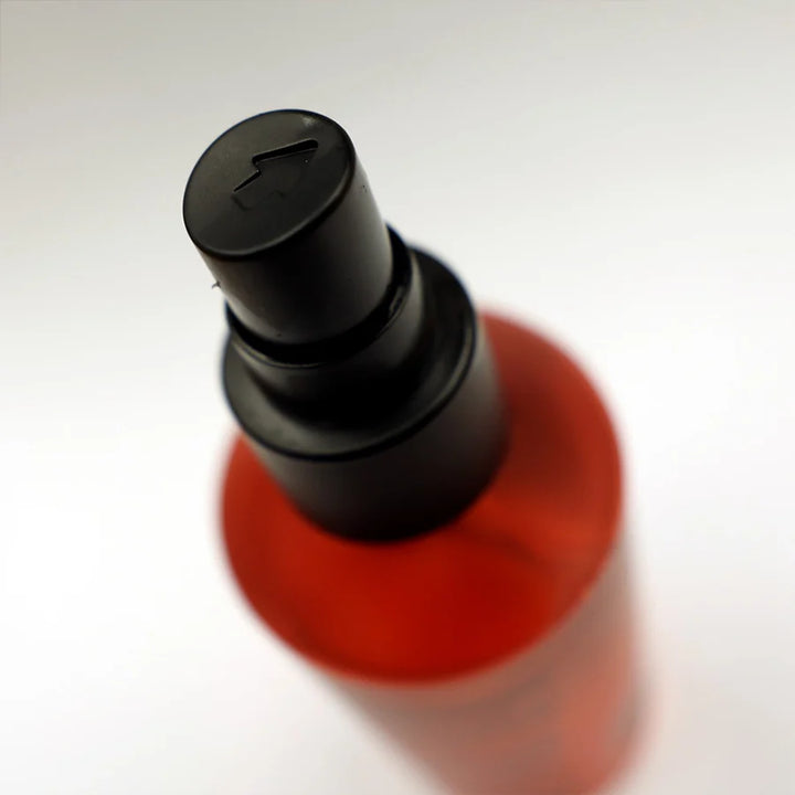 Gros plan sur le pulvérisateur noir du Clay Spray Uppercut Deluxe, vue du dessus avec embout spray et flacon rouge flou en arrière-plan