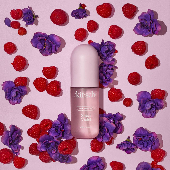 Parfum capillaire KITSCH Sheer Violet entouré de framboises rouges et de fleurs violettes sur fond rose, illustrant son profil floral fruité gourmand.