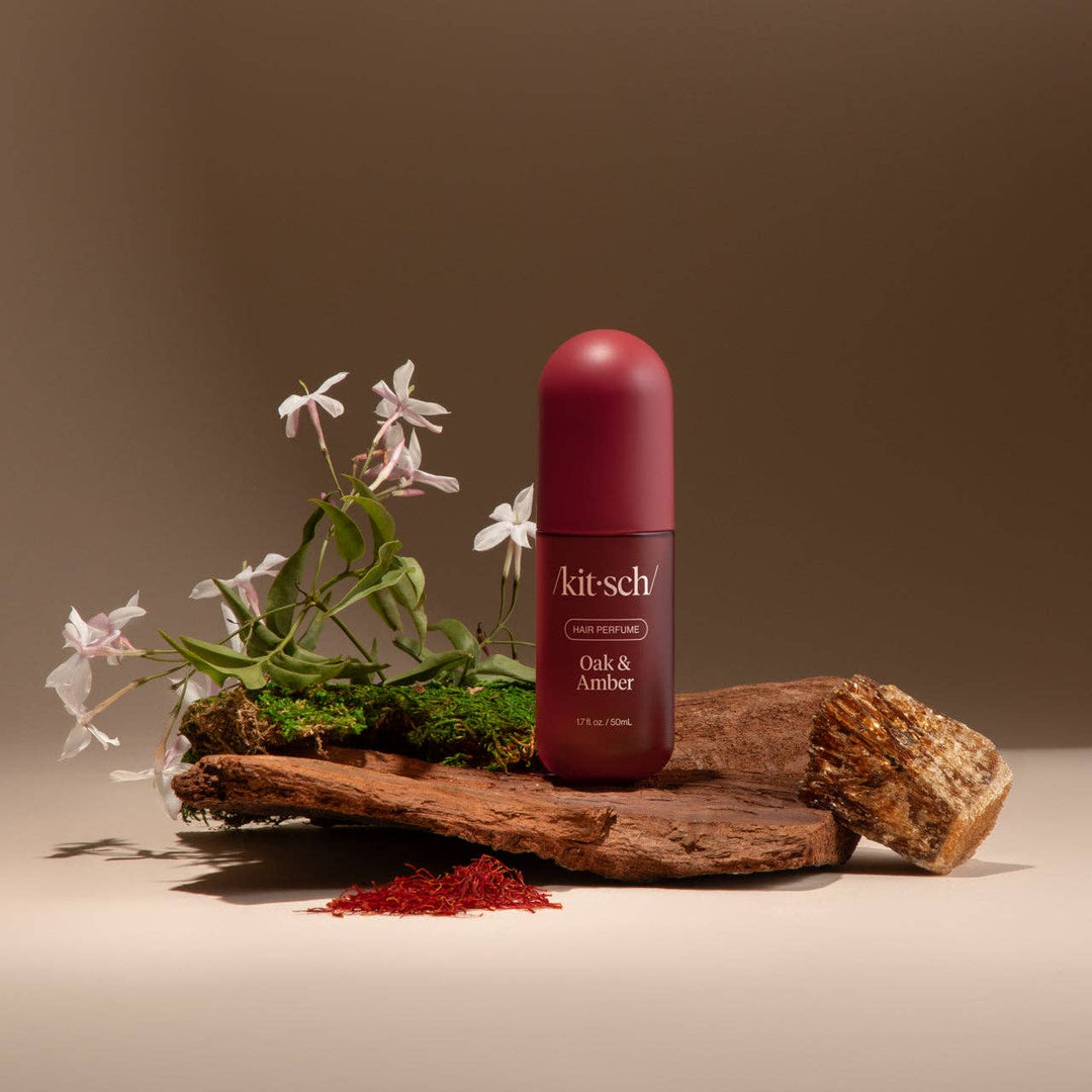 Parfum pour cheveux KITSCH Chêne & Ambre 50 ml posé sur de la mousse naturelle, du bois et des fleurs blanches, évoquant une fragrance boisée, élégante et chaleureuse