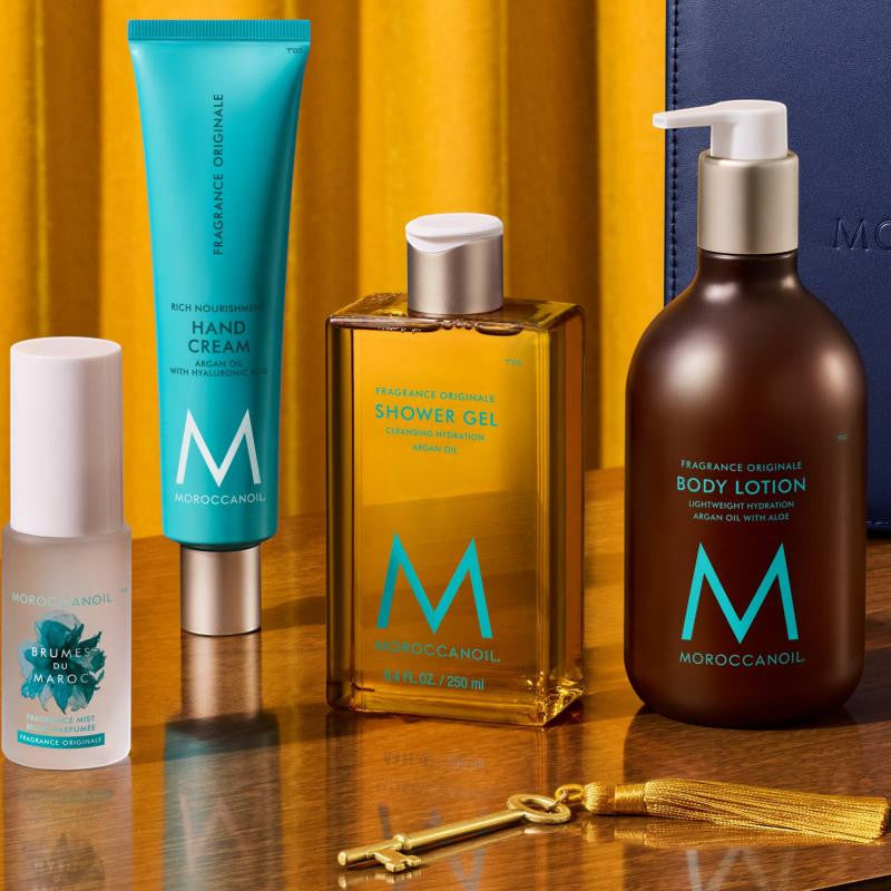 Soins corporels Moroccanoil Fragrance Originale comprenant Brumes du Maroc, crème mains, gel douche et lotion pour le corps sur décor doré.