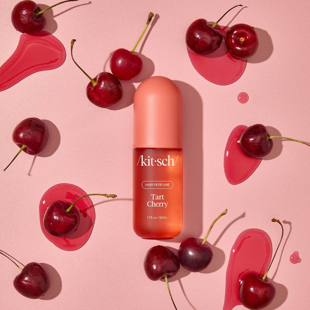 Parfum pour cheveux KITSCH Cerise Acidulée (Tart Cherry) 50 ml présenté avec des cerises fraîches sur fond rose. Flacon rose corail évoquant une fragrance gourmande et fruitée.