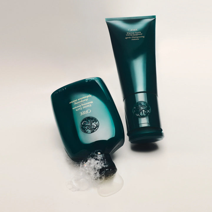 Shampooing et après-shampooing Oribe Eternal Curls pour cheveux bouclés présentés ensemble avec texture mousse visible du soin capillaire.