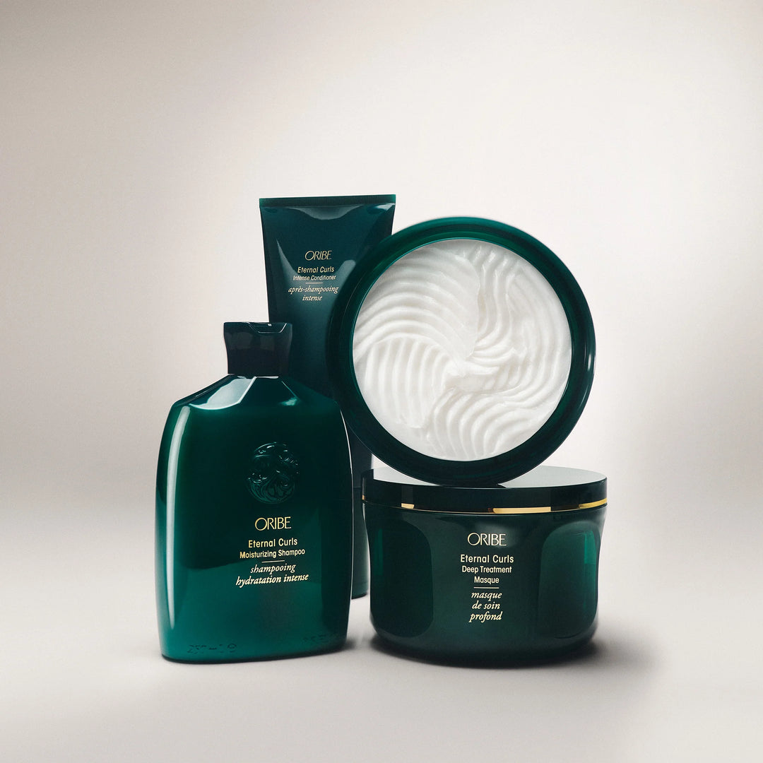 Produits Oribe Eternal Curls incluant shampooing hydratant, revitalisant intense et masque profond pour cheveux bouclés avec texture du soin visible.
