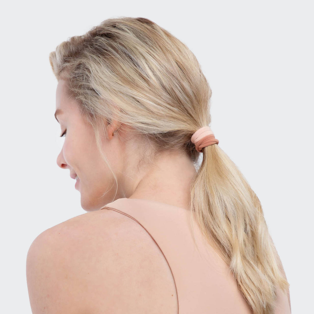 Femme portant un élastique KITSCH rose poudré dans une queue de cheval basse, accessoire cheveux écologique et sans couture sur fond beige.