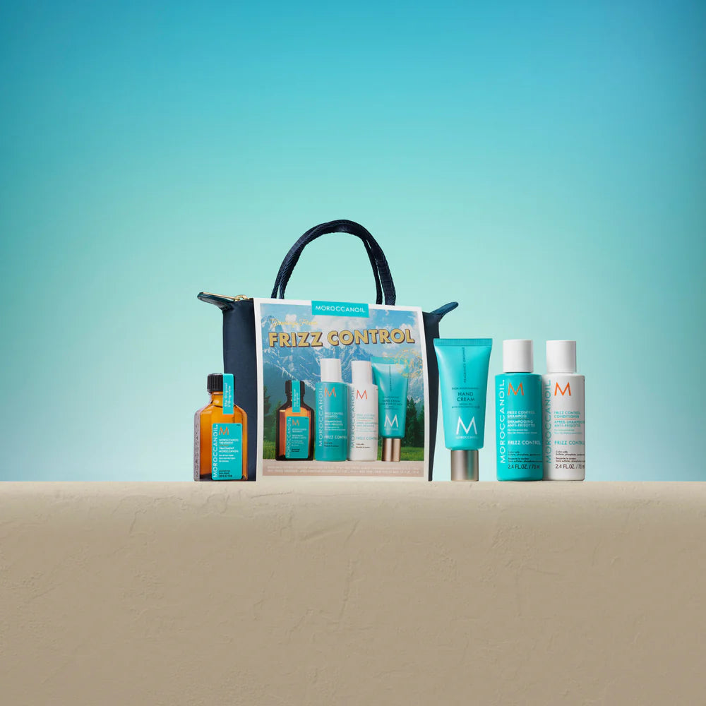 Coffret Moroccanoil Frizz Control dans une pochette bleu marin avec huile Moroccanoil, shampoing anti-frisottis, revitalisant et crème pour les mains disposés à côté sur une surface beige devant un fond turquoise.