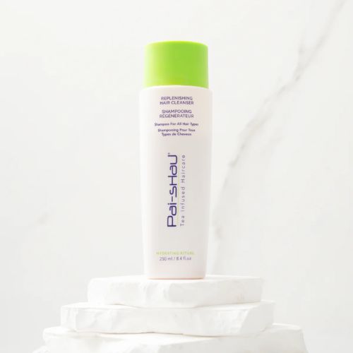 Flacon blanc mat de 250 ml du Shampoing Régénérateur Pai-Shau avec bouchon vert lime, posé sur des pierres blanches, sur fond marbré clair. Soin lavant végétalien hydratant pour cheveux colorés ou naturels.