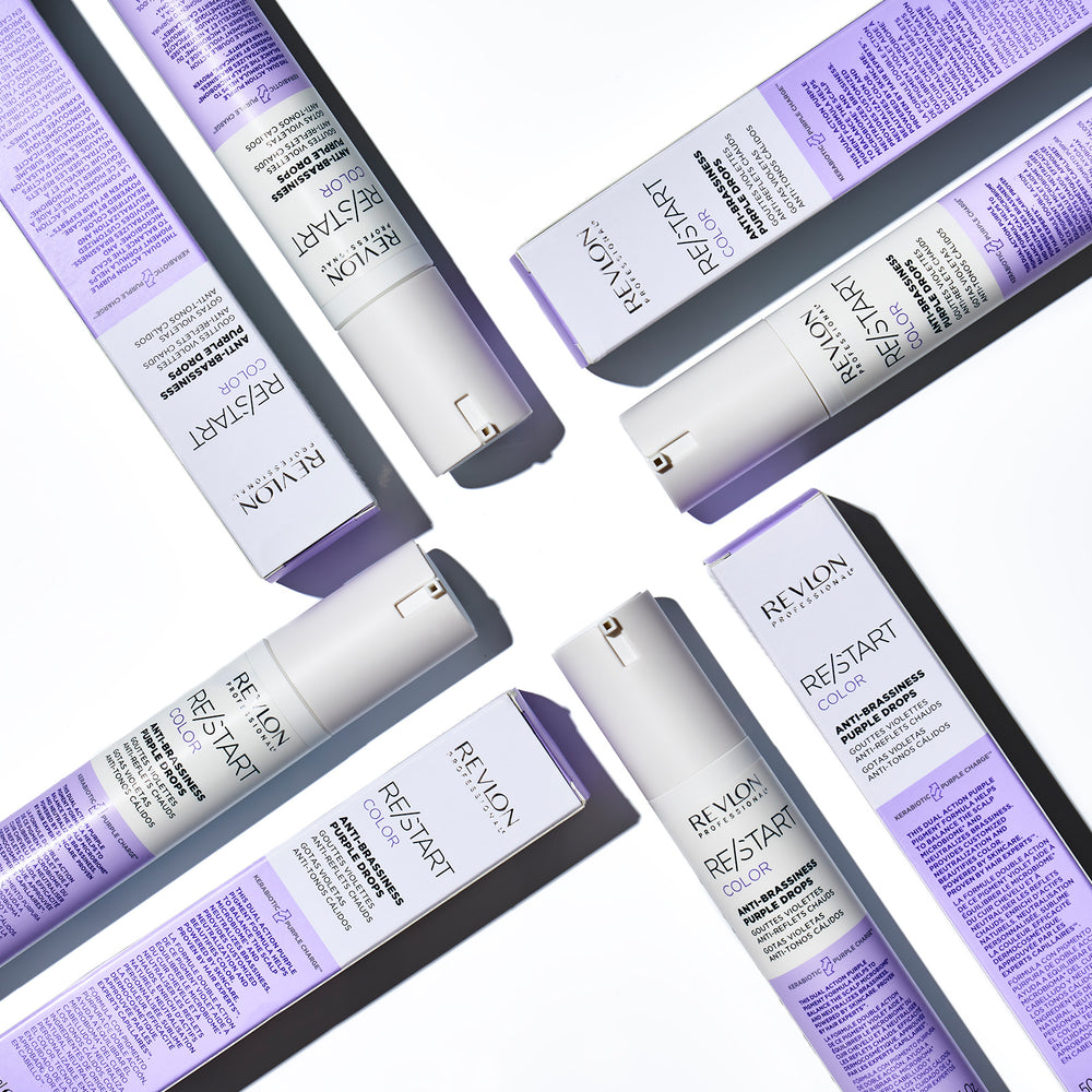 Produits REVLON Restart Color Anti-Brassiness Purple Drops disposés à plat avec leurs boîtes blanches et lilas sur fond clair, soin violet professionnel pour neutraliser les reflets chauds des cheveux blonds.