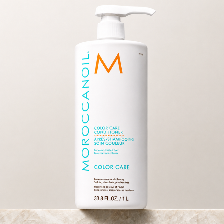 Après-shampoing Moroccanoil Soin Couleur 1 L pour cheveux colorés, grand flacon blanc avec pompe, logo turquoise et orange, présenté sur un fond beige professionnel.