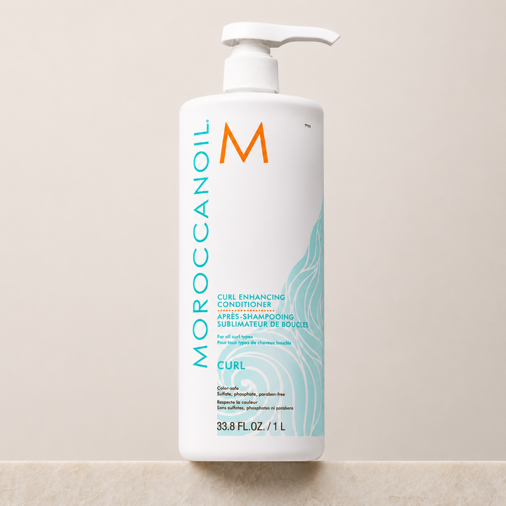 Après-shampoing Sublimateur de Boucles Moroccanoil 1 L en bouteille blanche avec pompe blanche, étiquette turquoise, photo produit professionnelle sur fond beige clair.