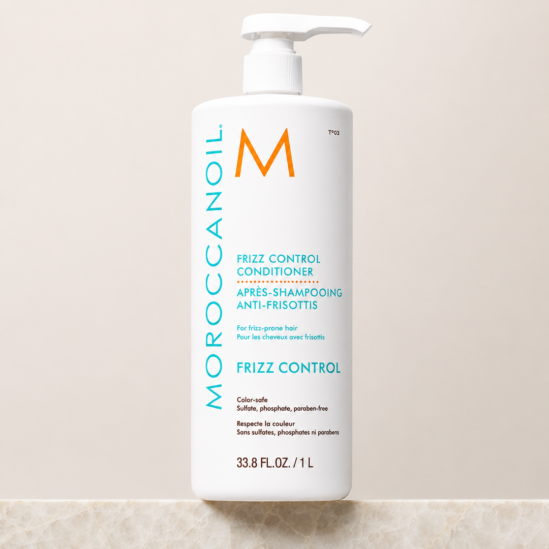 Après-shampoing anti-frisottis Moroccanoil 1 litre avec pompe blanche, bouteille grand format blanche, étiquette turquoise et orange, photographie professionnelle sur fond beige.