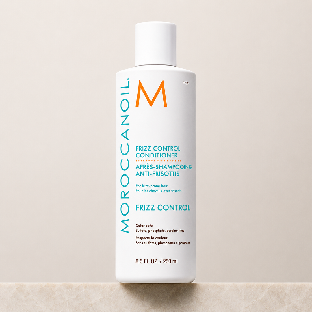 Après-shampoing anti-frisottis Moroccanoil 250 ml en bouteille blanche avec bouchon à vis, étiquette turquoise et orange, photographie produit sur fond beige avec comptoir effet marbre.