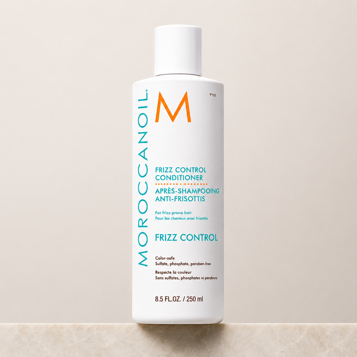 Après-shampoing anti-frisottis Moroccanoil 250 ml en bouteille blanche avec bouchon à vis, étiquette turquoise et orange, photographie produit sur fond beige avec comptoir effet marbre.