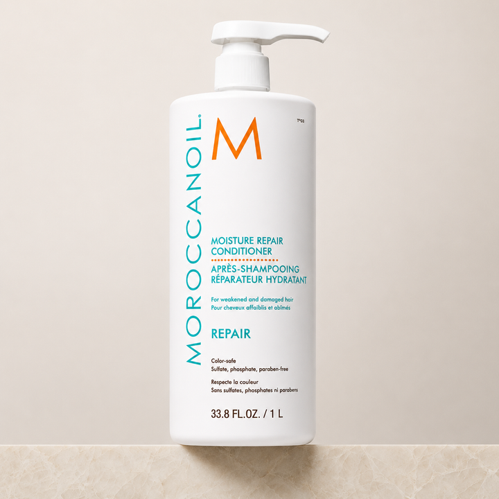 Après-shampoing réparateur hydratant Moroccanoil 1 L avec pompe blanche, bouteille blanche au design épuré, étiquette turquoise et orange, fond beige professionnel.