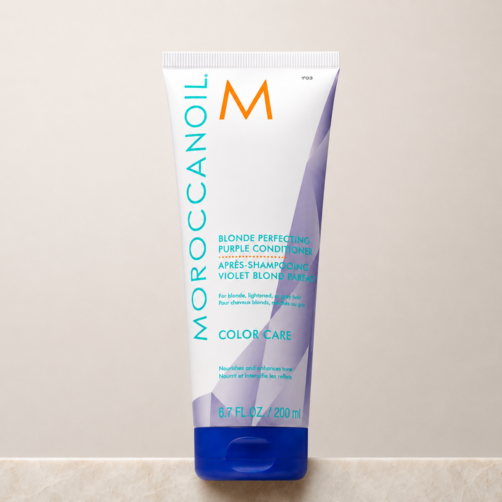 Après-shampooing Violet Blond Parfait Moroccanoil 200 ml en tube blanc avec bouchon bleu, accents violets et turquoise, photographié sur un comptoir en pierre avec fond beige en studio professionnel.