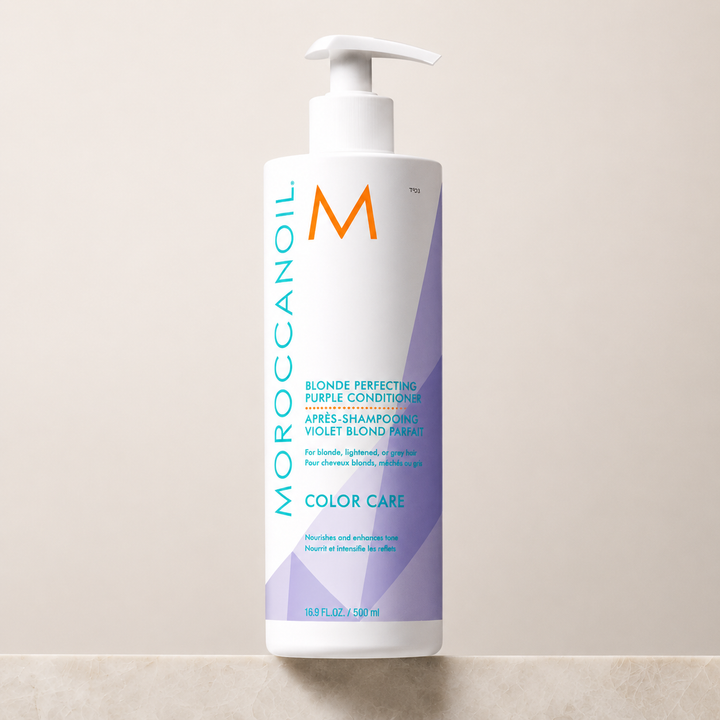 Après-shampooing Violet Blond Parfait Moroccanoil 500 ml avec pompe blanche, bouteille blanche aux accents violets et turquoise, présentée sur un comptoir en pierre avec fond beige minimaliste.