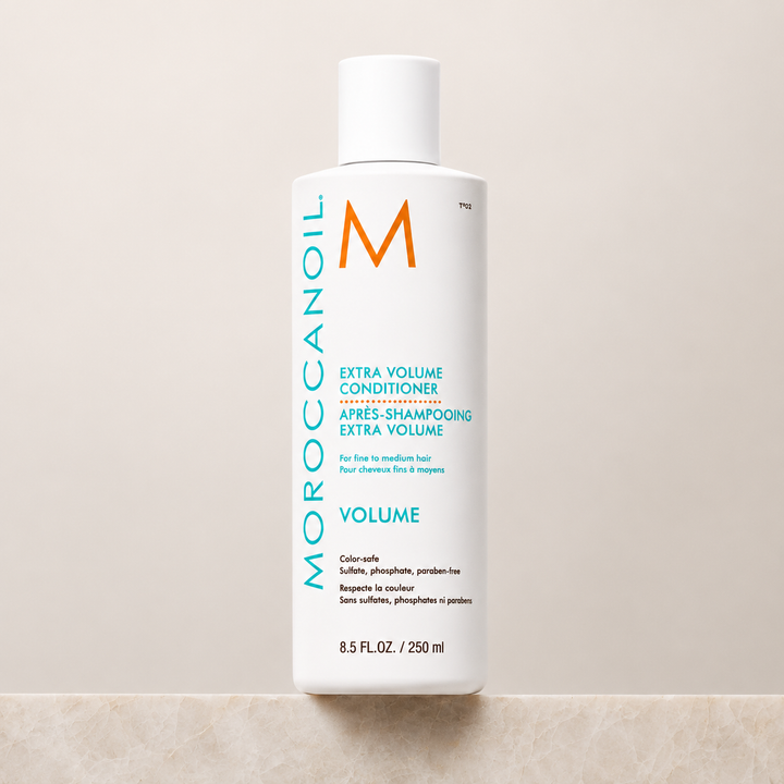 Après-shampoing Extra Volume Moroccanoil 250 ml en bouteille blanche avec bouchon blanc, étiquette turquoise et orange, revitalisant volumisant pour cheveux fins, présenté sur fond beige minimaliste.