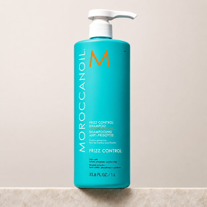 Shampoing Anti-Frisottis Moroccanoil 1 Litre en bouteille turquoise avec bouchon blanc, présenté sur fond beige. Soin capillaire professionnel hydratant qui contrôle les frisottis, protège de l'humidité et convient aux cheveux colorés.