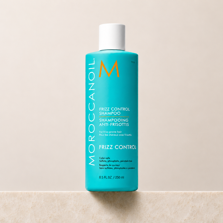 Shampoing Anti-Frisottis Moroccanoil 250 ml en bouteille turquoise avec bouchon blanc, présenté sur fond beige. Soin capillaire professionnel hydratant qui contrôle les frisottis, protège de l'humidité et convient aux cheveux colorés.