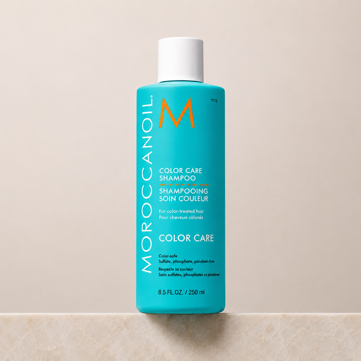 Shampoing Moroccanoil Color Care 250 ml en bouteille turquoise avec bouchon blanc, présenté sur un comptoir en pierre sur fond beige minimaliste, photo produit professionnelle.