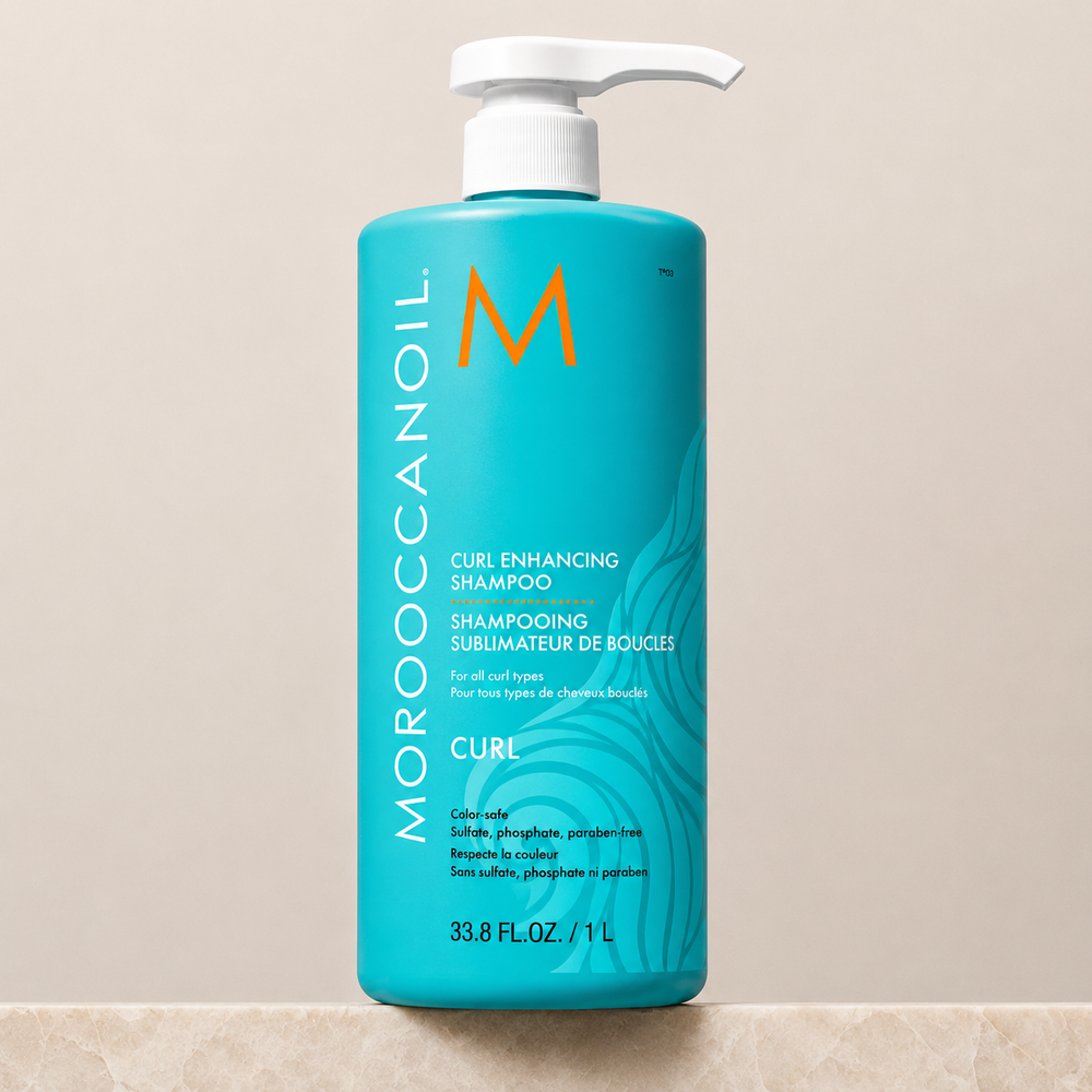 Shampoing Sublimateur de Boucles Moroccanoil 1 L en bouteille turquoise avec pompe blanche, fond beige épuré, soin hydratant pour cheveux bouclés, ondulés et frisés.