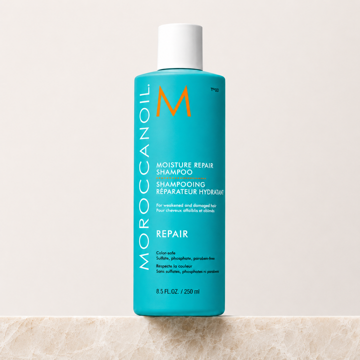 Bouteille turquoise Moroccanoil Shampoing Réparateur Hydratant avec bouchon blanc, format 250 ml , présentée sur fond beige clair. Soin capillaire réparateur à l’huile d’argan pour cheveux abîmés.