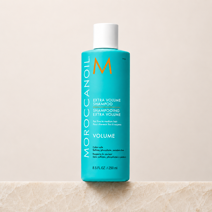 Shampoing Extra Volume Moroccanoil 250 ml  en bouteille turquoise avec bouchon blanc ou pompe blanche, étiquette blanche et orange, photo professionnelle sur fond beige, soin volumisant pour cheveux fins