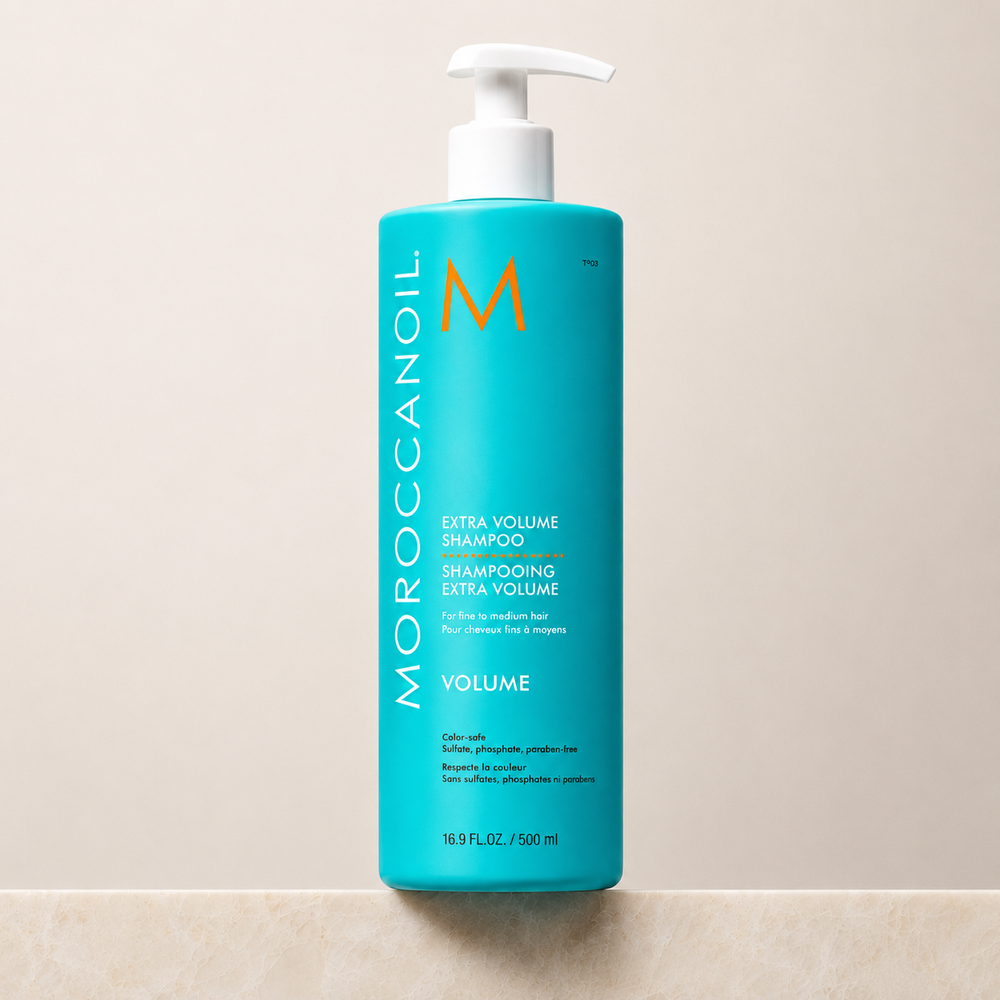 Shampoing Extra Volume Moroccanoil 500 ml en bouteille turquoise avec bouchon blanc ou pompe blanche, étiquette blanche et orange, photo professionnelle sur fond beige, soin volumisant pour cheveux fins