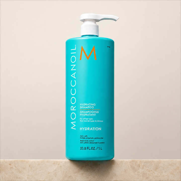 Shampoing hydratant Moroccanoil 1 L en bouteille turquoise avec pompe blanche, fond beige épuré, soin hydratant pour cheveux.