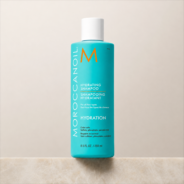 Shampoing hydratant Moroccanoil 250 ml en bouteille turquoise avec bouchon blanc, fond beige minimaliste, photo produit professionnelle pour cheveux bouclés.
