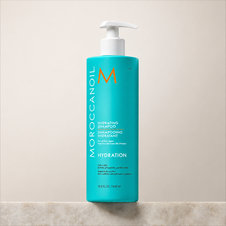 Shampoing hydratant Moroccanoil 500 ml en bouteille turquoise avec pompe blanche, fond beige épuré, soin hydratant pour cheveux.